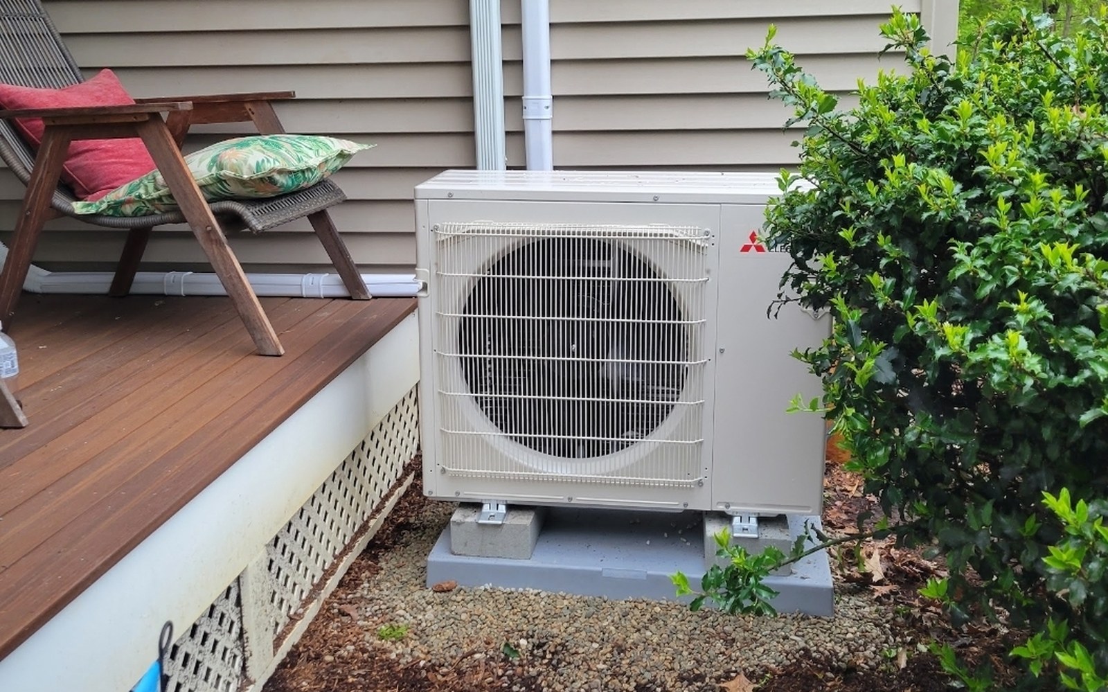 Mitsubishi heat pump installed on a level gravel pad beside a home's deck