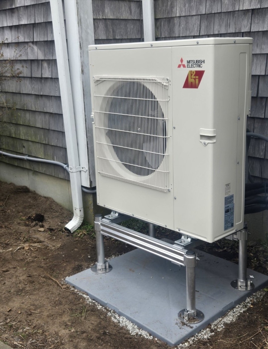 Mitsubishi Electric H2i outdoor unit raised on a riser stand against cedar shake siding